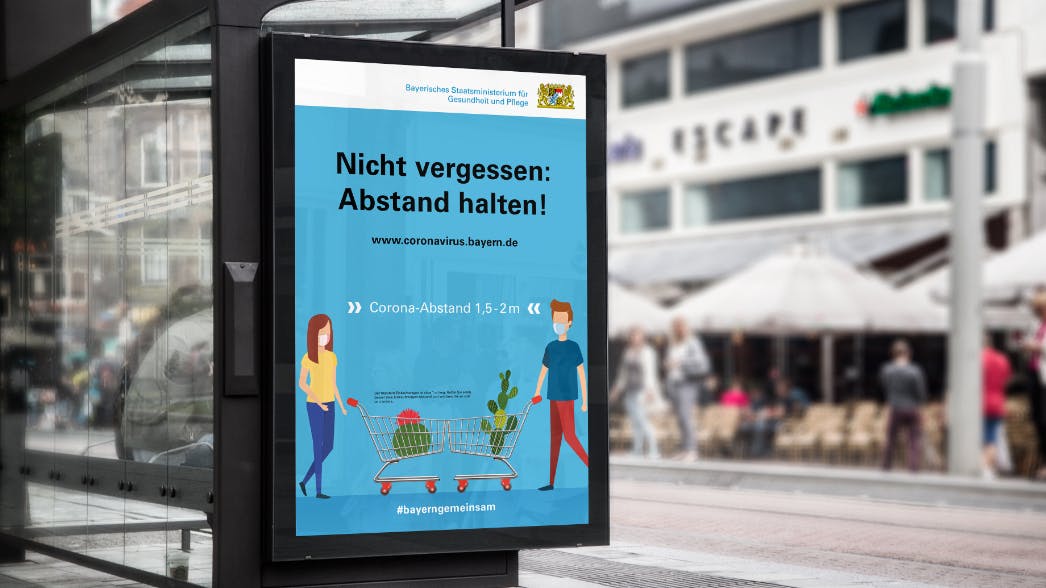 Krisenkommunikation COVID-19: Kampagne auf vielen medialen Kanälen. Hier ein buntes Plakat zu den Abstandsregelungen an einer Haltestelle in München.